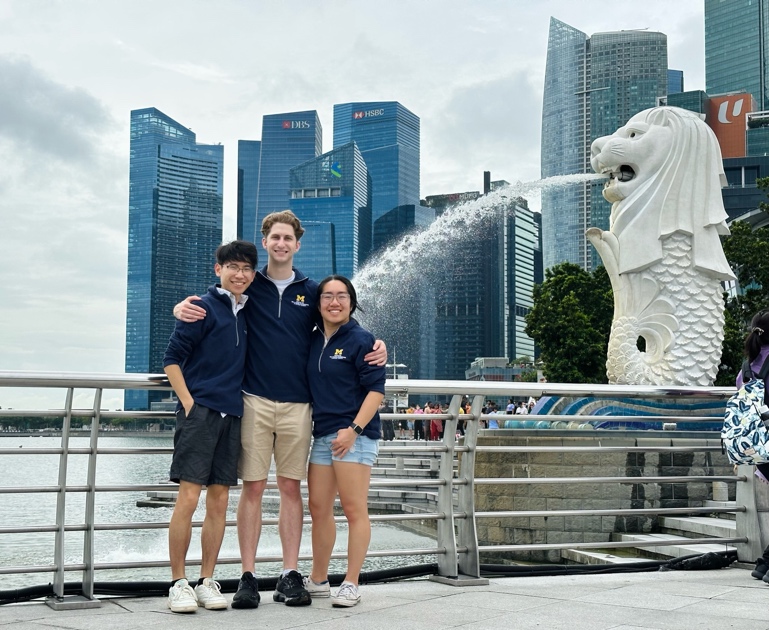Fumiya Abe-Nornes, Nathan Smith, and Rachel Zhang standing on a bridge next to a statue of a sea lion spouting water