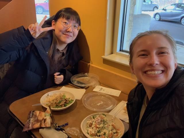 Yanru and Caroline smile at the camera while seated with their food at a booth at Panera Bread