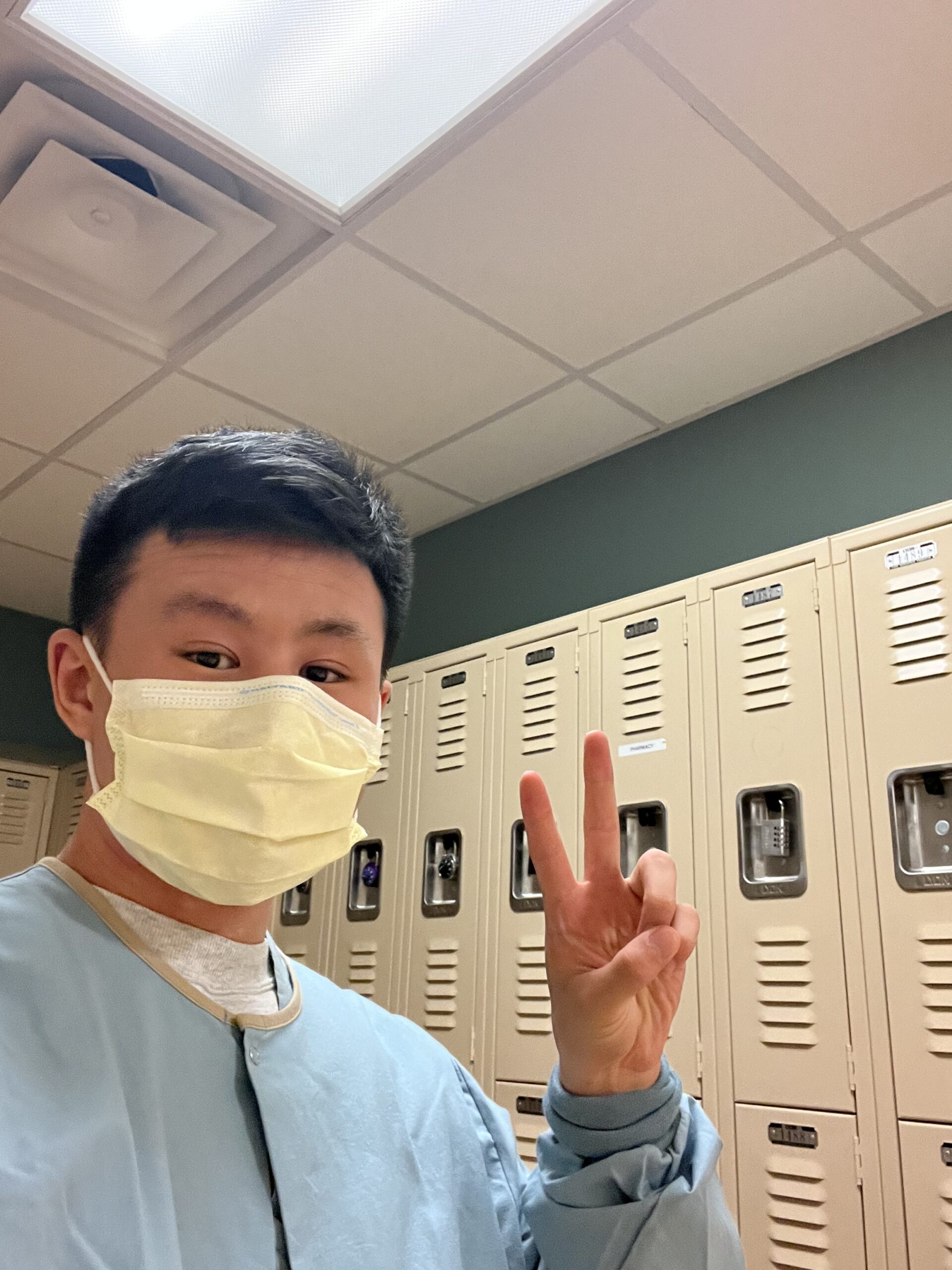 Josh holding a peace sign to the camera while wearing a paper mask and scrubs.