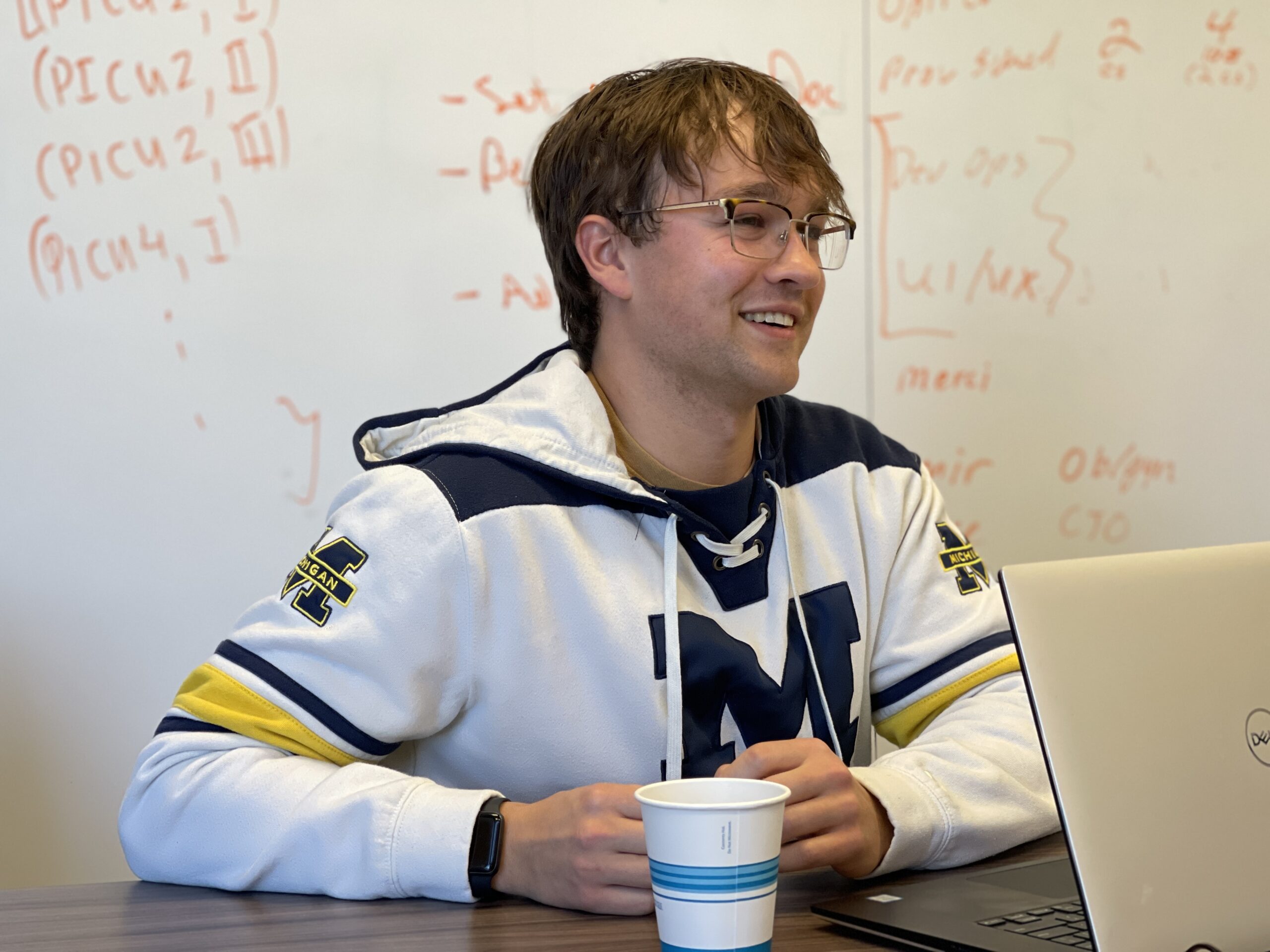 Close-up photo of Jared smiling in a conference room while wearing a Michigan hockey jersey.